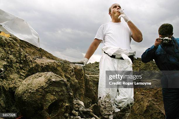 Worker smokes a cigarette in a mass grave containing the bodies of men massacred in Srebrenica in July 1995 that has been opened and the bodies are...