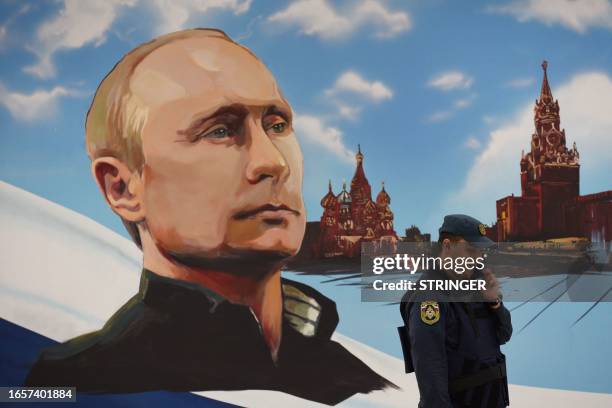 Russian rescuer speaks on his mobile phone next to a wall bearing an image of Russia's President Vladimir Putin and Moscow's Kremlin at a polling...