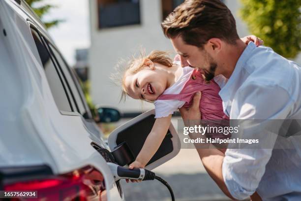 father and his daughter charging their electric car on the street. - elektrische auto stockfoto's en -beelden