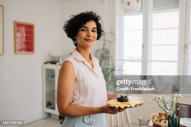 donna latinoamericana sorridente in piedi vicino al tavolo da pranzo, tenendo un tagliere di formaggio - donna piatto foto e immagini stock