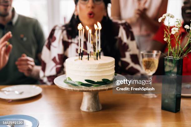 joven anónima celebra su cumpleaños entre amigos, soplando velas en pastel de cumpleaños - vela de cumpleaños fotografías e imágenes de stock