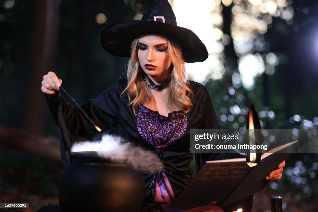 The fantasy woman witch conjures, holds a magic wand and a magic book in her hands, and reads spell white magic smoke from boiling vat. Halloween theme. Witch performs ceremony on Halloween day