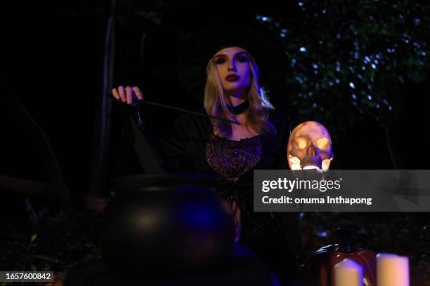 the fantasy woman witch conjures, holds a magic wand and a magic book in her hands, and reads spell white magic smoke from boiling vat. halloween theme. witch performs ceremony on halloween day - witch wand stock pictures, royalty-free photos & images