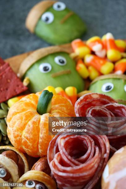 close-up image of cheese-charcuterie board, frankenstein monster kiwi fruit, salami roses, candy corn, pumpkin seeds, crackers, sausage mummies, satsuma pumpkins, grey background, focus on foreground - frankenstein stock pictures, royalty-free photos & images