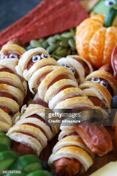 full frame image of cheese-charcuterie board, sausage mummies, pumpkin seeds, cucumber, crackers, cheddar, satsuma pumpkin, focus on foreground - frankenstein stock pictures, royalty-free photos & images