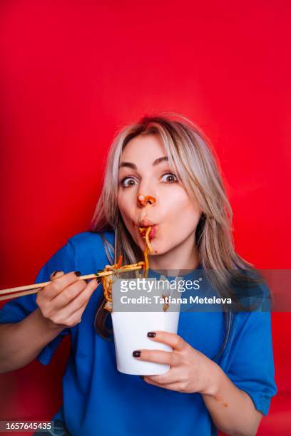 funny woman smeared in sauce sucking noodles from box using chopsticks and look at camera - funny fat women stockfoto's en -beelden