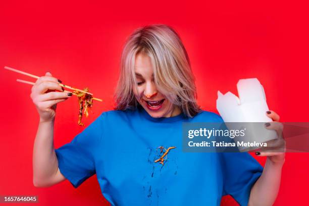 chopstick noodle adventure: messy blonde woman diving into flavorful world of asian wok noodles with saucy hands and shirt in a red studio - white shirt stain stock pictures, royalty-free photos & images