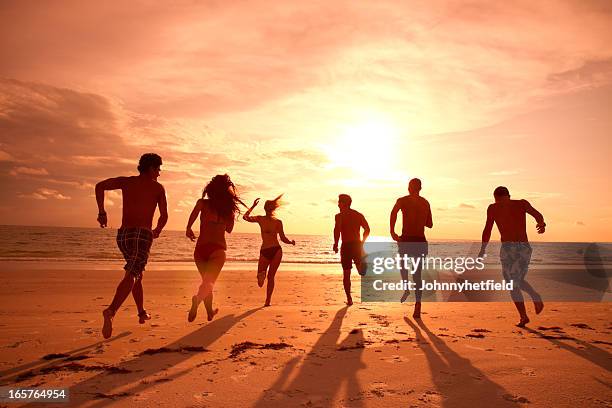 group of friends running on the beach at sunset - spring break stock pictures, royalty-free photos & images