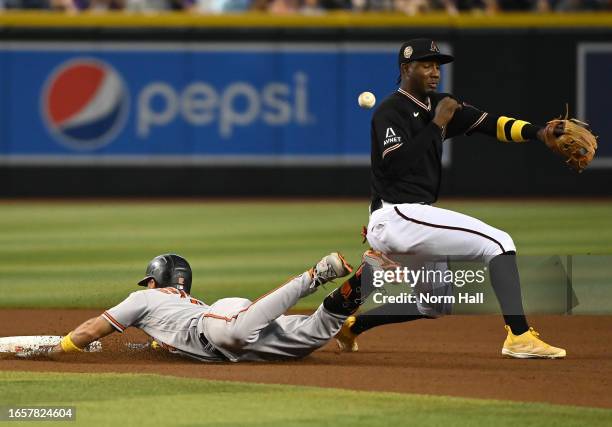 Geraldo Perdomo of the Arizona Diamondbacks cannot make a play on a throw from Alek Thomas as Adam Frazier of the Baltimore Orioles slides safely...