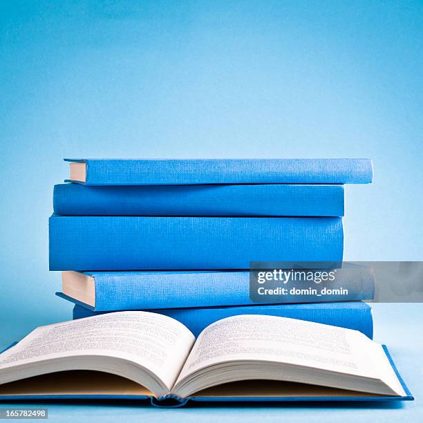 aperto il libro contro pila di libri isolato su sfondo blu - book on table foto e immagini stock