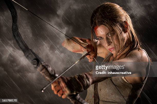 female heroine with bow and arrow on a rainy night - pijl en boog stockfoto's en -beelden
