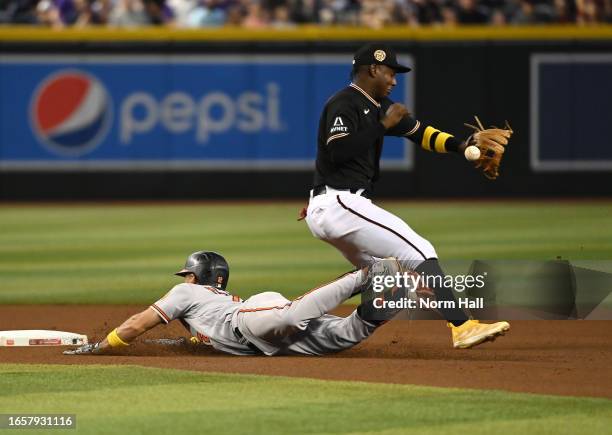 Geraldo Perdomo of the Arizona Diamondbacks cannot make a play on a throw from Alek Thomas as Adam Frazier of the Baltimore Orioles slides safely...