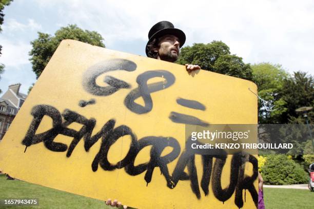 Protestor holds a placard reading "G8 = Democratur" a contraction of French words "democratie" and "dictature" as he takes part in a demonstration,...
