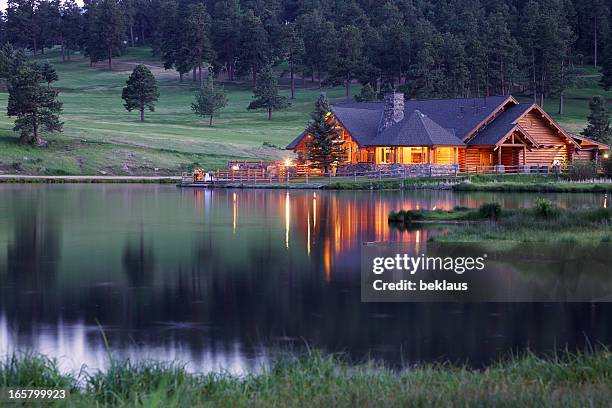 mountain lodge que refleja en el lago al atardecer - árbol de hoja perenne fotografías e imágenes de stock