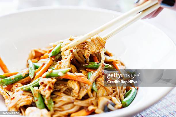woman's hand uses chopsticks to serve thai chicken noodle dish - stir fried noodles with chicken stock pictures, royalty-free photos & images