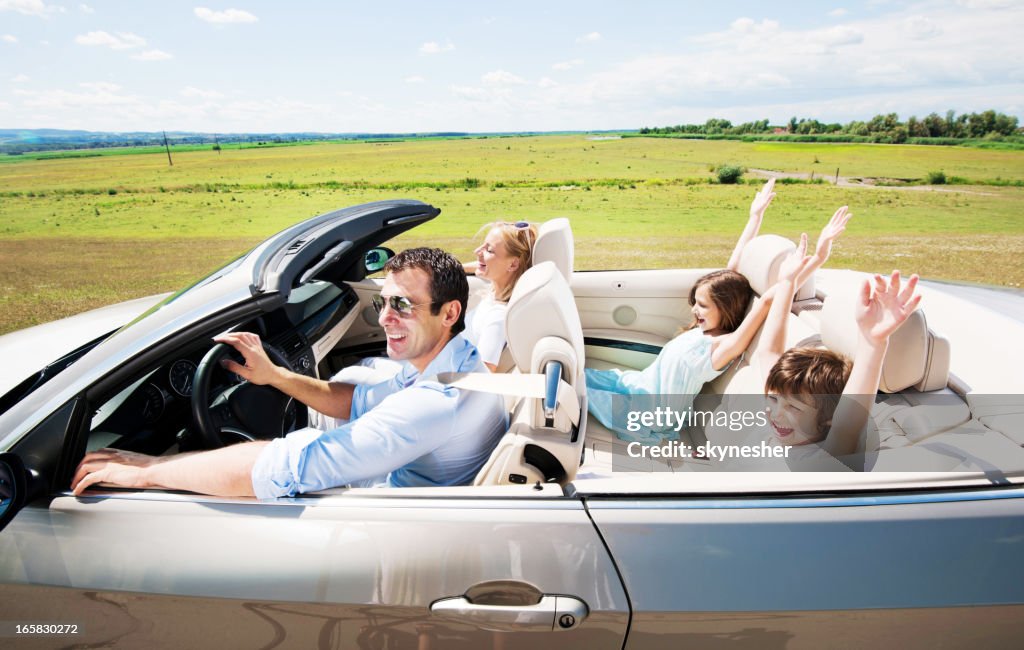 Happy family driving in a convertible car.