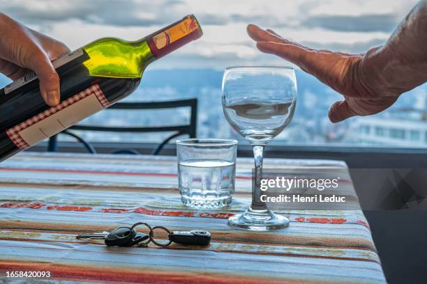 hand of a man refusing red wine and showing car keys and a glass of water on a table at home - rubbing alcohol stock-fotos und bilder