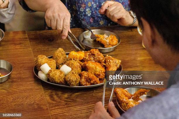 In this photo taken on June 13 customers use tongs to serve themselves fried chicken that was cooked by a robot, at a Robert Chicken restaurant in...