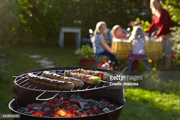 barbecue grill on a summer evening with family in background - family barbeque garden stock pictures, royalty-free photos & images