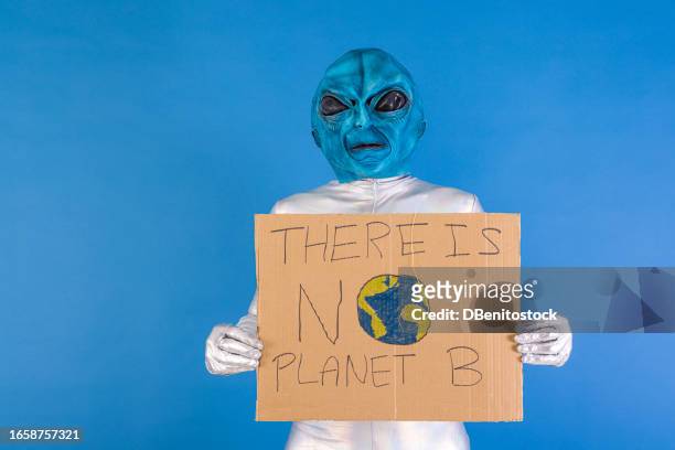 person dressed in a blue allan mask and metallic suit holding a cardboard sign with letters that read: 'there is no planet b'. destruction, planet, apocalypse, sustainability and care for the planet. - et poster stockfoto's en -beelden