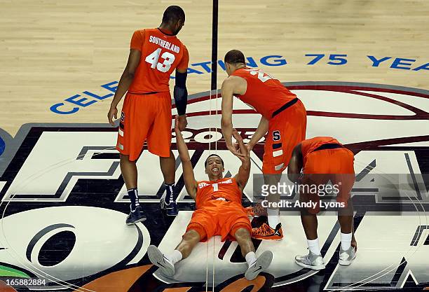 Michael Carter-Williams of the Syracuse Orange is helped up off of the court by teammates James Southerland and Brandon Triche of the Syracuse Orange...