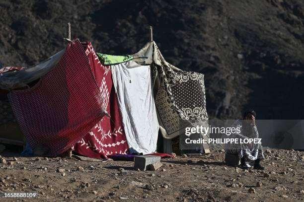 Woman sits outside her makeshift shelter in the mountain village of Moulay Brahim in the central province of Al-Haouz, on September 11, 2023. The...