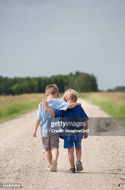 two boys walking down a gravel road - arm around shoulder behind stock pictures, royalty-free photos & images
