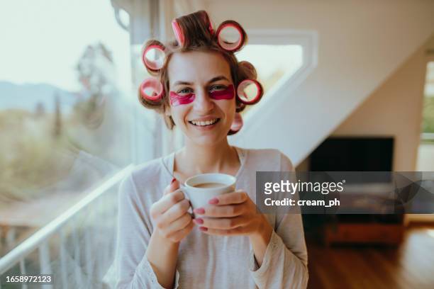 frau mit haarwicklern und augenmaske trinkt morgens zu hause kaffee - hair curlers stock-fotos und bilder