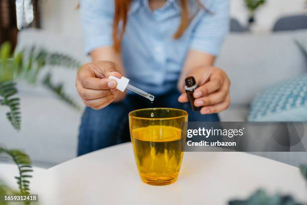 young woman putting medicine drops in a glass of water - dropper bottle stock pictures, royalty-free photos & images