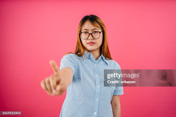 unzufriedene frau, die mit dem finger vor einem rosa hintergrund winkt - verbotsschild stock-fotos und bilder