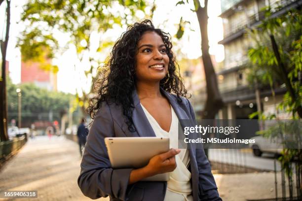 empresaria latina positiva caminando por la ciudad - empresa de carácter social fotografías e imágenes de stock