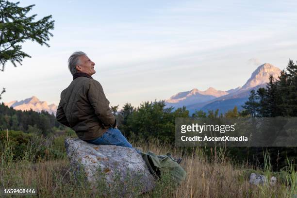 reifer männlicher wanderer entspannt sich bei sonnenaufgang auf der wiese - confidence male landscape stock-fotos und bilder