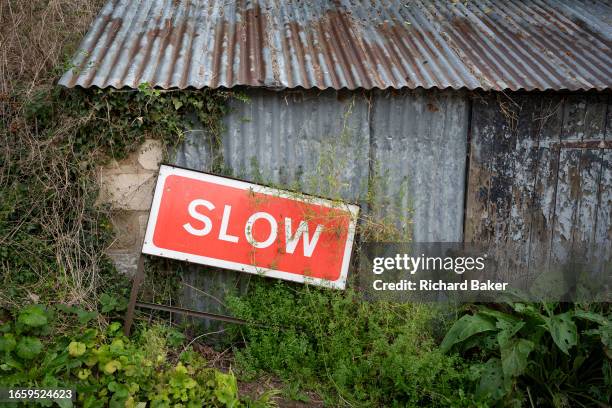 Slow down sign rests against a corrugated iron shed in the Cotswolds village of Sheepscombe, on 8th September 2023, near Stroud, England. Since the...