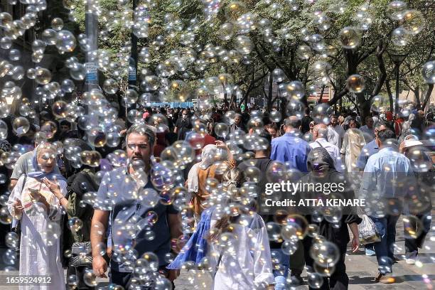 Bubbles blown by a merchant surround people walking outside the Grand Bazaar in Tehran on September 5, 2023. A year after the death of Mahsa Amini...