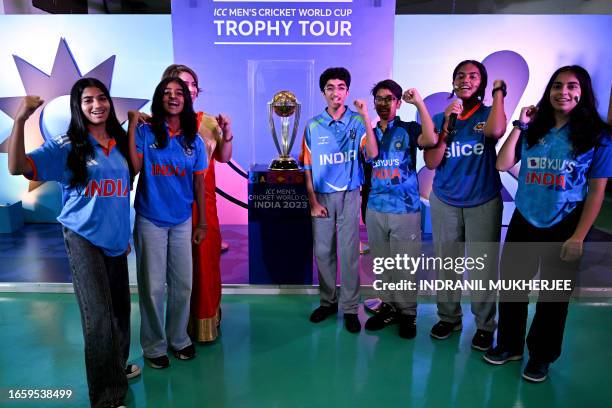 Students pose for a picture next to the ICC Men's Cricket World Cup 2023 trophy on display at a school as part of an official trophy tour in Mumbai...