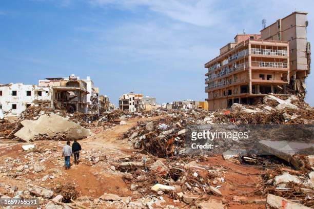 Men walk past debris of buildings caused by flash floods in Derna, eastern Libya, on September 11, 2023. Flash floods in eastern Libya killed more...