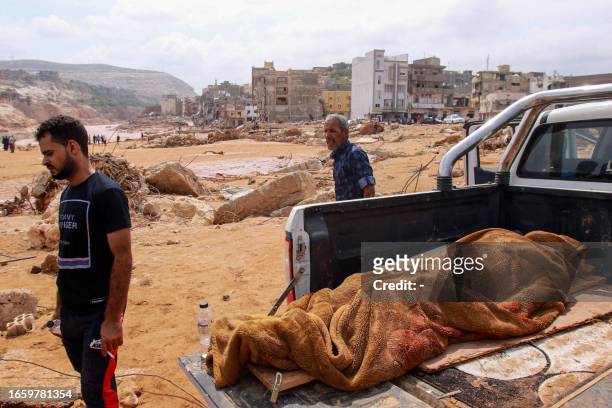 Graphic content / TOPSHOT - People walk past the body of a flash flood victim in the back of a pickup truck in Derna, eastern Libya, on September 11,...