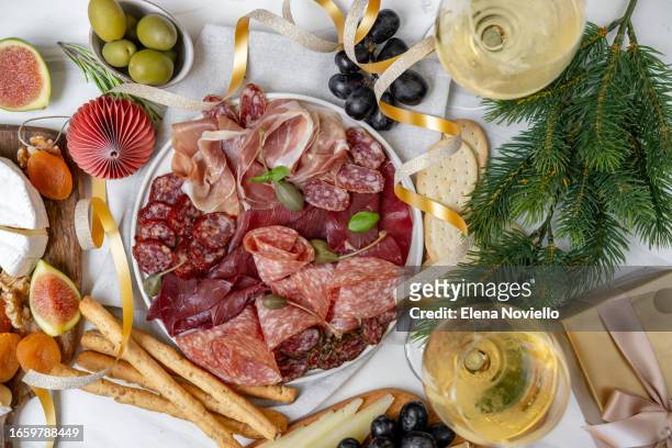 christmas appetizer table lunch meat italian prosciutto ham, parma ham, salami, bresaola beef and olives, cheese board and grissini breadstick. charcuterie plate. two glasses of white wine or prosecco and festive decor - aperitief stockfoto's en -beelden