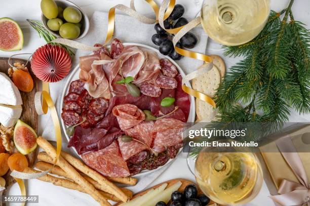 christmas appetizer table lunch meat italian prosciutto ham, parma ham, salami, bresaola beef and olives, cheese board and grissini breadstick. charcuterie plate. two glasses of white wine or prosecco and festive decor - appetiser stock pictures, royalty-free photos & images