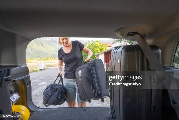 mature woman loading her bags for the road trip in the trunk of the car. - possession stock pictures, royalty-free photos & images