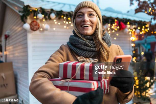 young woman with christmas presents, using smart phone - christmas smartphone stock pictures, royalty-free photos & images