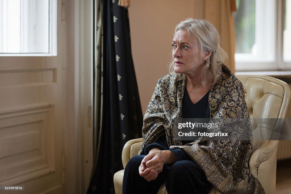 Senior Frau sitzt alleine im Wohnzimmer und sieht traurig