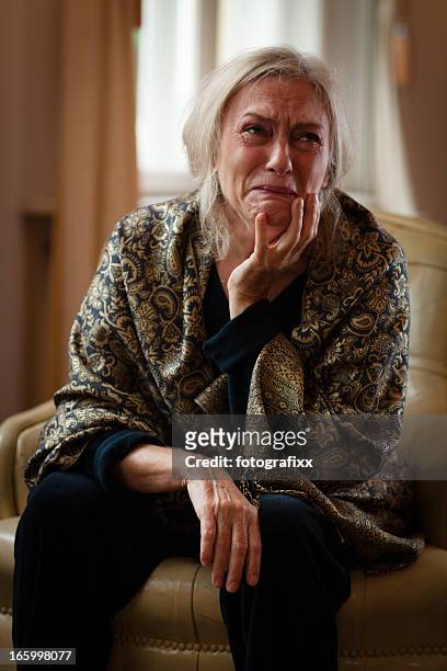 senior woman sits alone in living room and cry - woman crying stock pictures, royalty-free photos & images