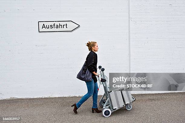 woman pushing baggage cart under german exit sign - vorbeigehen stock-fotos und bilder