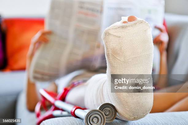 femme avec une jambe cassée allongée sur le canapé et la lecture d'un journal - broken heel photos et images de collection