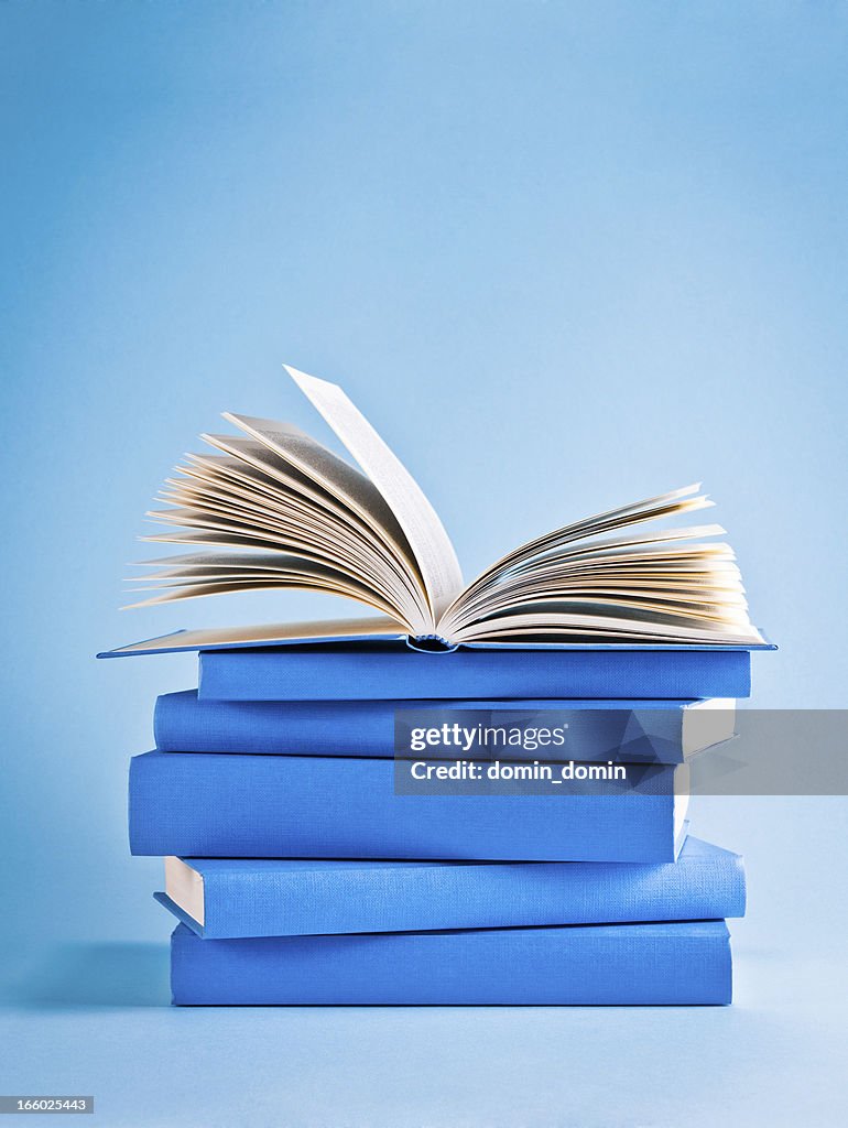 Opened book on top of stack of blue books, knowledge