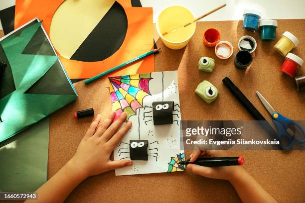 above view of a girl's hand drawing with felt-tip pen spiders for halloween decoration. - halloween craft stock pictures, royalty-free photos & images