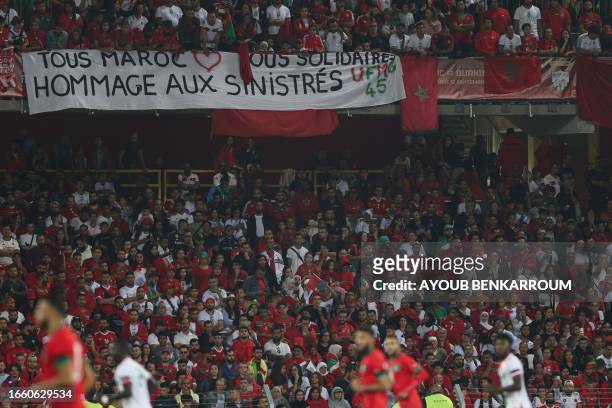 Supporters hold a banner reading "All Morocco, all suportive, tribute to all victims" during the international friendly football match between...