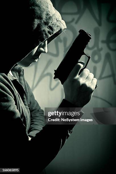 man in hood with revolver - villain stock pictures, royalty-free photos & images