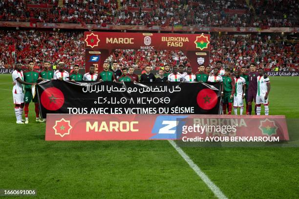 Morocco, Burkina Faso players and match officals hold a banner in solidarity for the victims of the Moroccan earthquake ahead of the international...